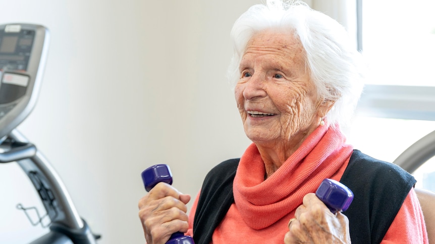 An elderly woman smiling and holding weights in her hands.