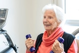 An elderly woman smiling and holding weights in her hands.