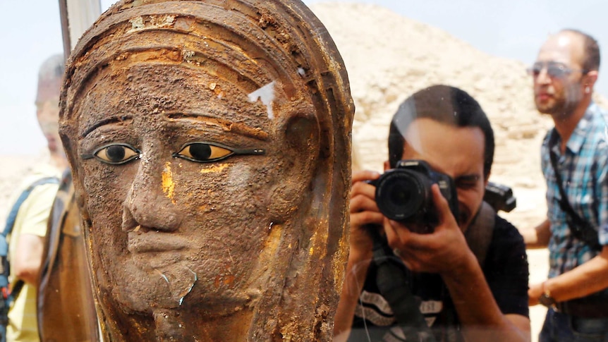 A photographer points his camera at a gilded silver mummy mask.
