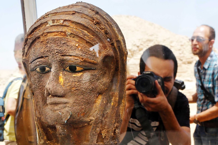 A photographer points his camera at a gilded silver mummy mask.