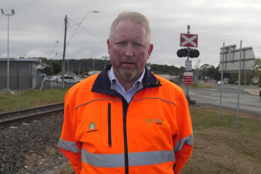 A man in high-vis stands in front of a train track.
