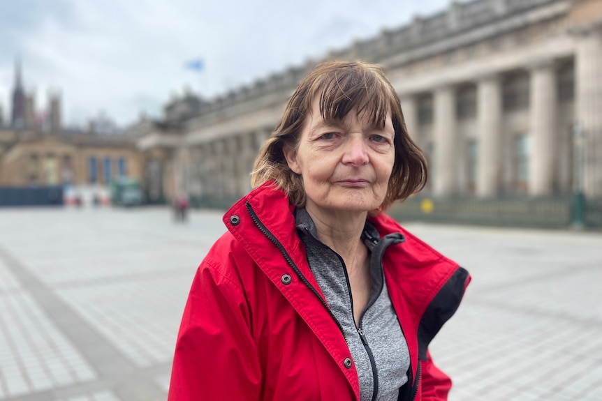 Una vecchia con una giacca rossa si trova in una piazza di Edimburgo.