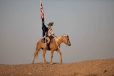 A lone horseman carries the Australian flag in the outback as the sun sets.
