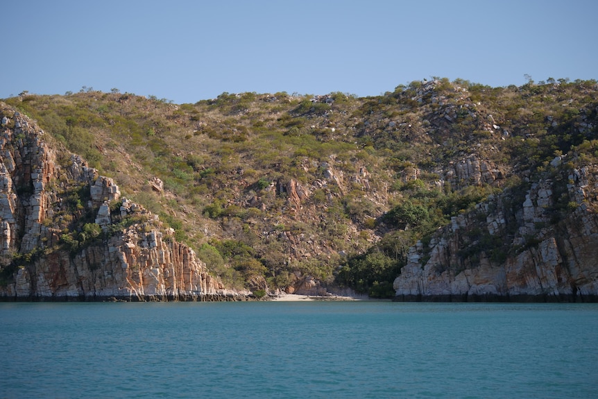 A bay with blue water against large cliffs covered with green vegetation.