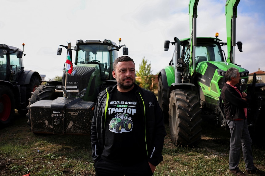 Man stands in front of a line of tractors. 