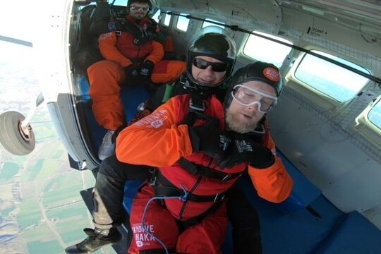 A man, strapped to someone else, in a plane about to fall out while skydiving