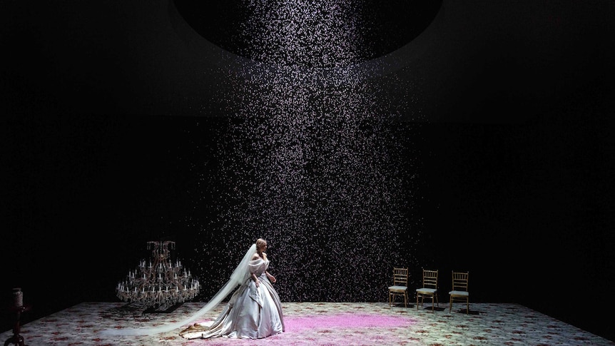Eryn Jean Norvill walks across a carpeted stage in a wedding dress as pink confetti rains down from the ceiling.