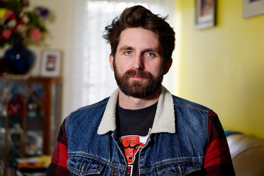 Man wearing denim jacket in a room with yellow walls. 