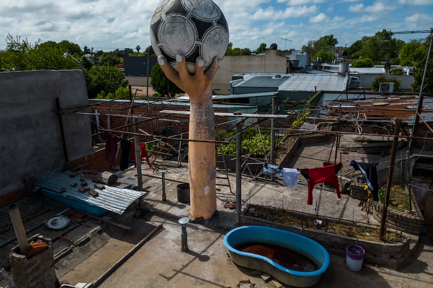A sculpture of an arm holding a soccer ball on the roof of a house. 