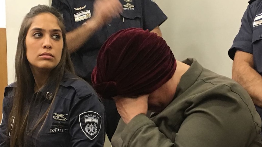 A woman surrounded by law enforcement officers holds her face in her hand.