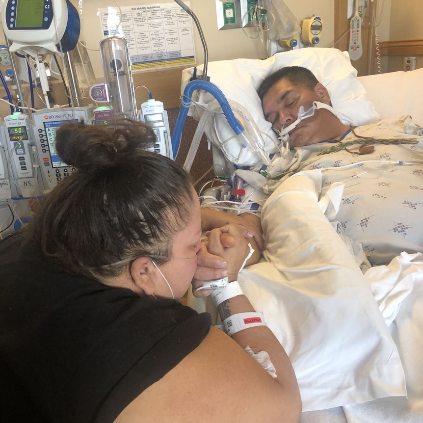 Woman holding the hand of her husband in hospital, kissing his hand.