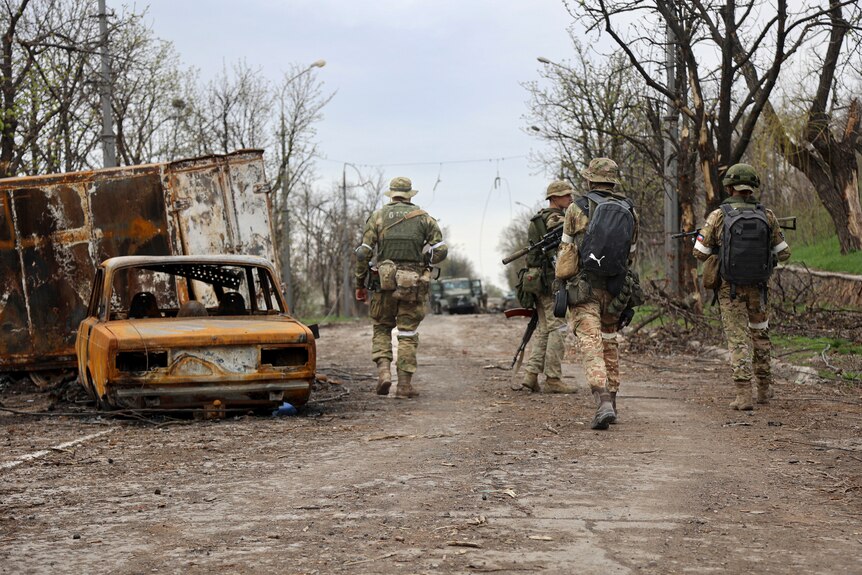 Los militares pasan junto a los vehículos dañados en Mariupol.