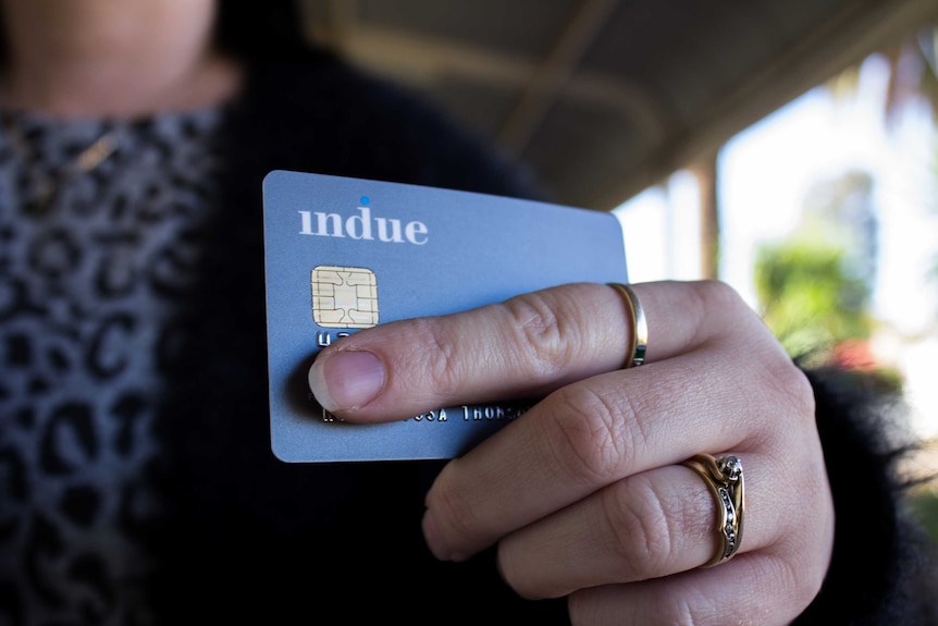 A grey bank card held in a woman's hand. She wears wedding and engagement rings, and ring on forefinger.