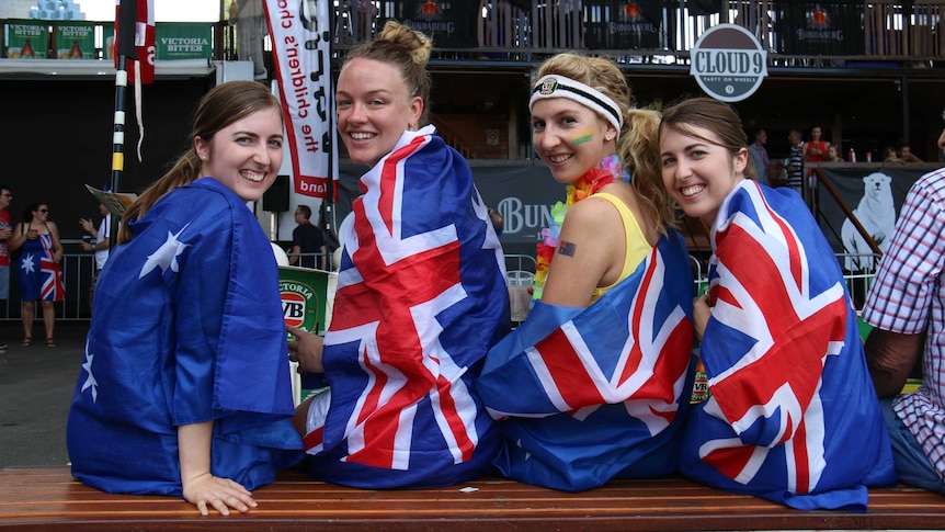 Four young women draped in Australian flags sit on a bench at a bar.