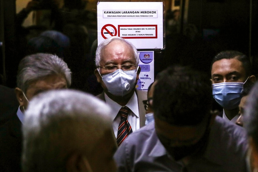 Prime Minister Najib Razak, centre, arrives at the Kuala Lumpur High Court complex wearing a face mask surrounded by people.