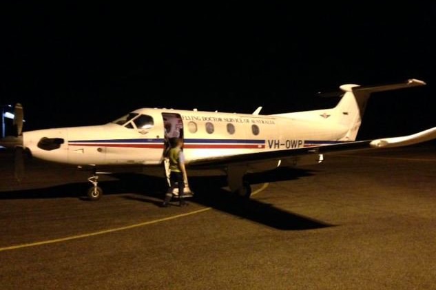An RFDS plane sits on the tarmac at an airport in darkness.