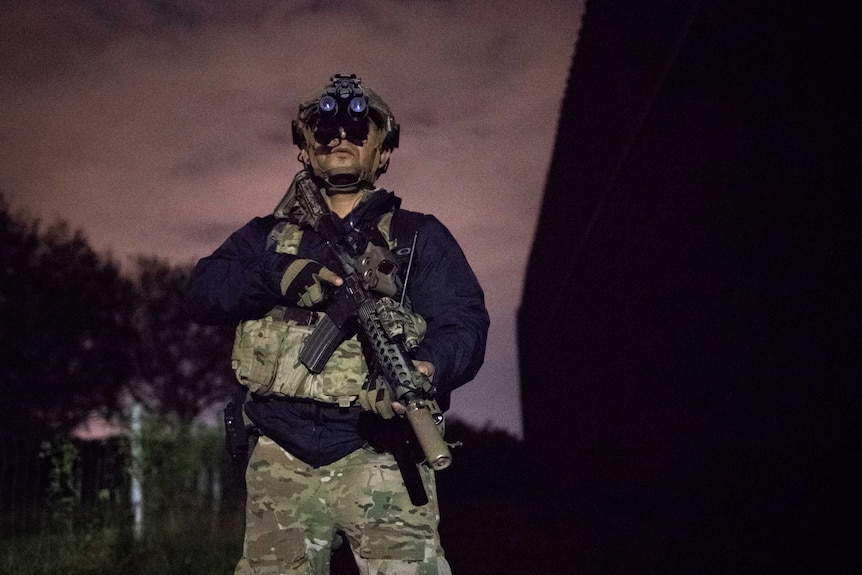 A man carrying a gun in heavy camouflage gear in the dark