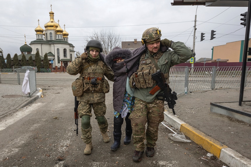 Ukrainian servicemen help carry an elderly woman