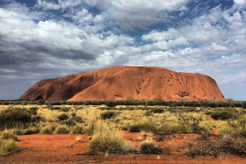 Uluru against blue skies dotted with cloud.