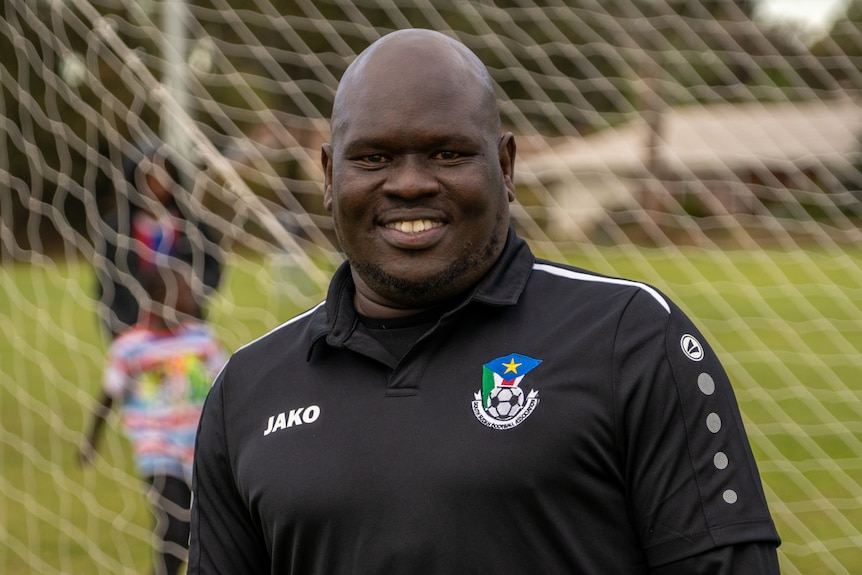 An African man standing in front of soccer goals smiles at the camera