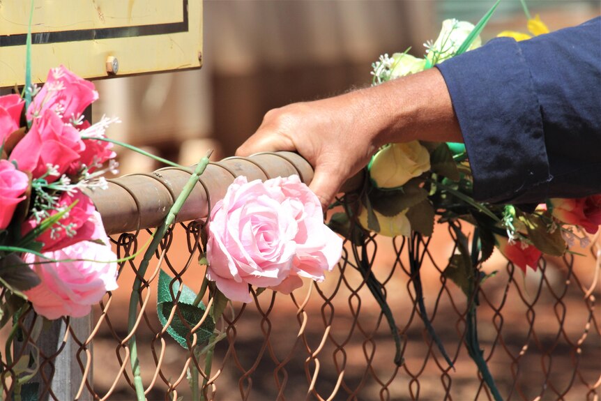 A hand grips the fence next to a flower