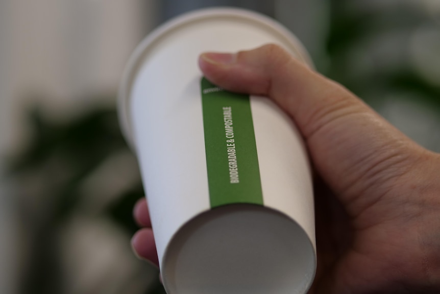 A hand holding a disposable coffee cup on an angle with the words biodegradable and compostable written on the side