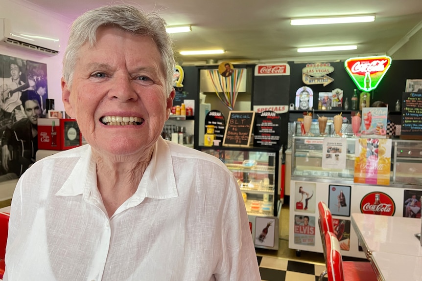 A woman in a shirt smiles at the camera in front of old retro signs in a diner.