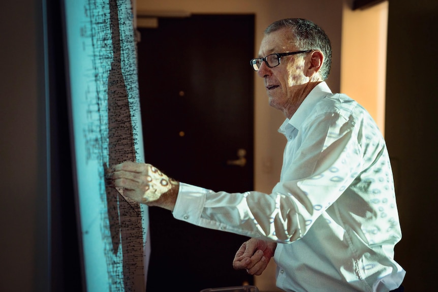 A middle-aged white man with short hair, a white shirt and glasses working on an art installation