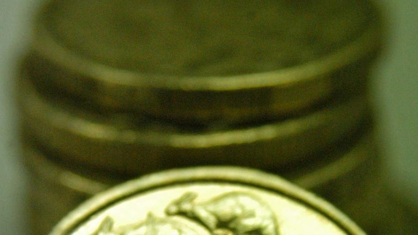 As Australian one dollar coin sits against a stack of other Australian one dollar coins