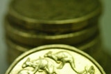 An Australian one dollar coin sits against a stack of other Australian one dollar coins