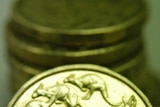 As Australian one dollar coin sits against a stack of other Australian one dollar coins