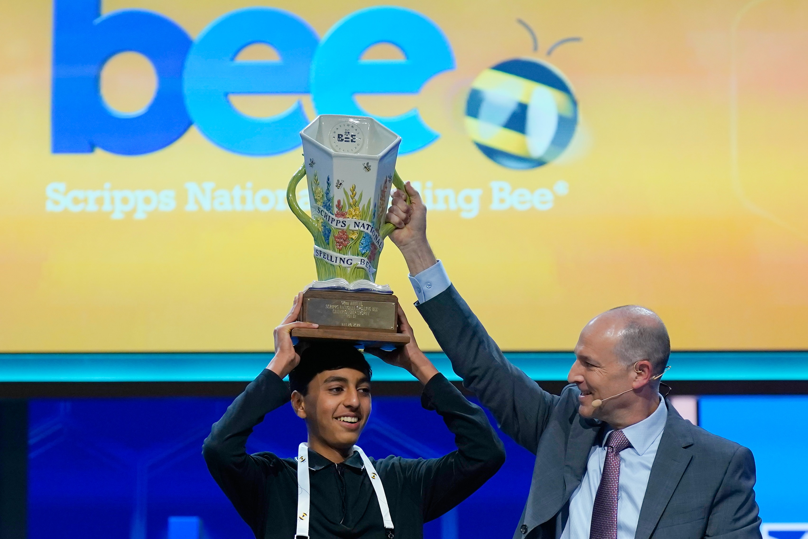 Un adolescente sostiene un trofeo en la cabeza junto al director del evento.