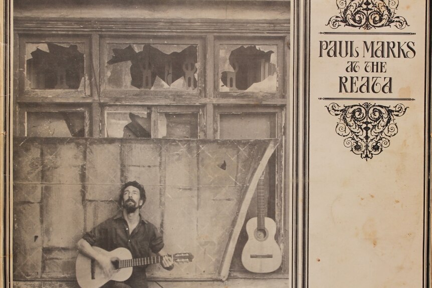 Marks poses with a guitar on the cover of his LP, sitting on the window sill of a dilapidated building