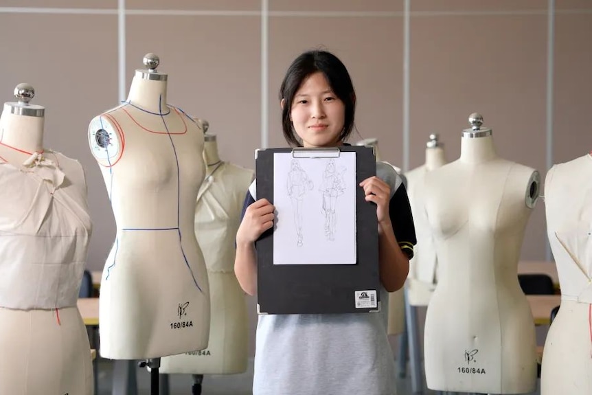 An Asian girl standing next to clothes models. 