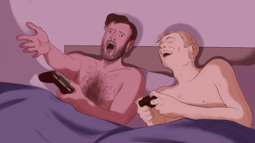 two guys lying in bed having fun and playing video games with no shirts on