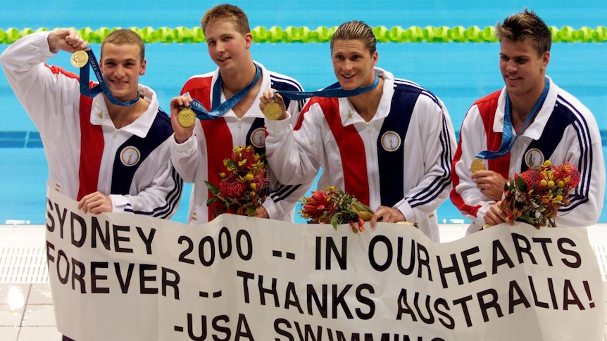 A group of American swimmers with gold medals hold a banner "Sydney 2000 In Our Hearts Forever Thanks Australia USA Swimming
