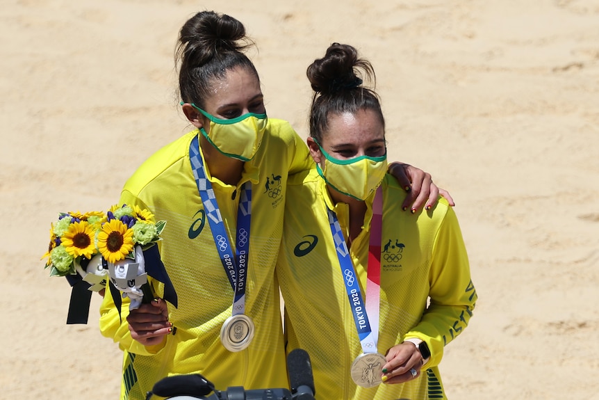 Two women wearing yellow tracksuits with silver medals around their necks