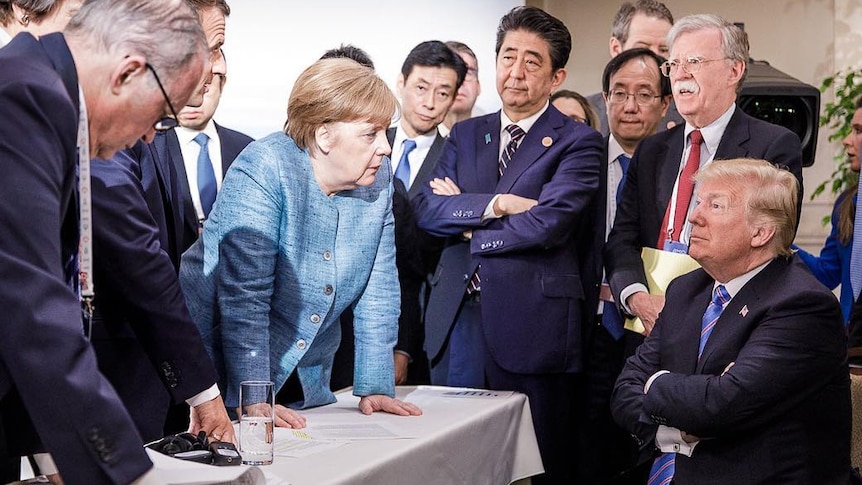 German Chancellor Angela Merkel surrounded by G7 leaders looking at Donald Trump