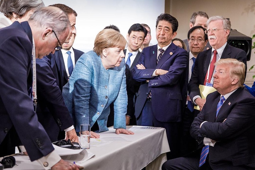 German Chancellor Angela Merkel surrounded by G7 leaders looking at Donald Trump