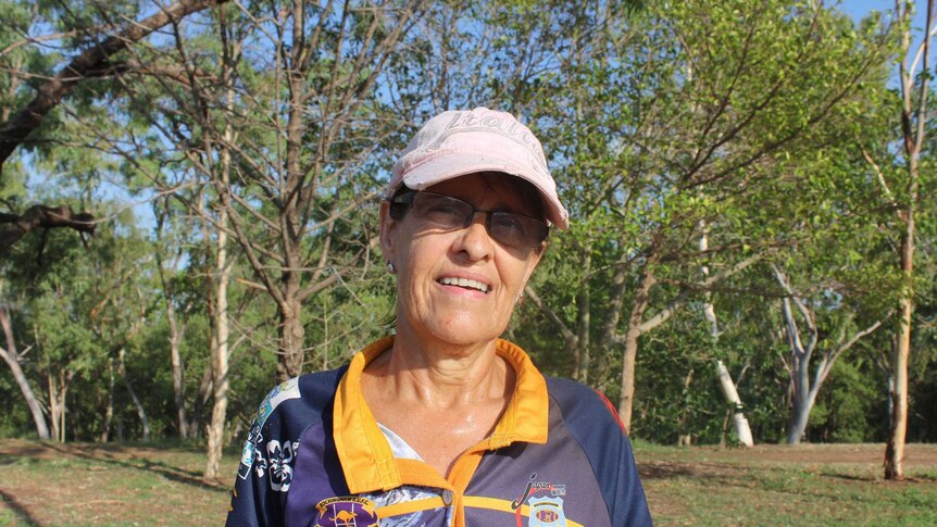 A woman in her sixties in gym gear and a sun visor standing before a grassland.