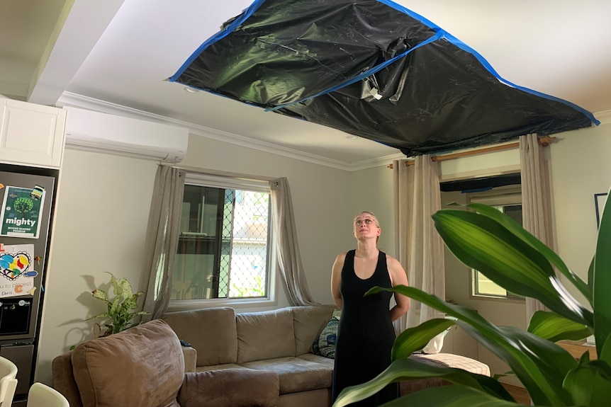 a woman in a house looking up at a ceiling covered in building tarp