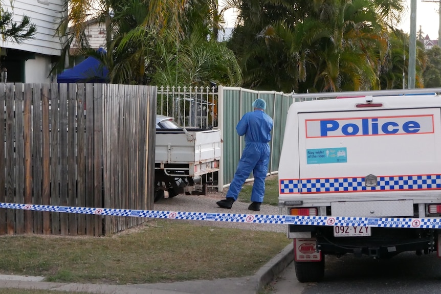 A police vehicle and an officer behind a cordoned-off home in suburbia.
