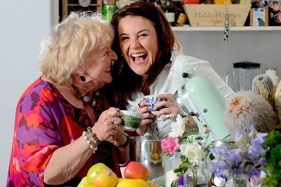 An old woman and a middle age woman holding tea cups and laughing.