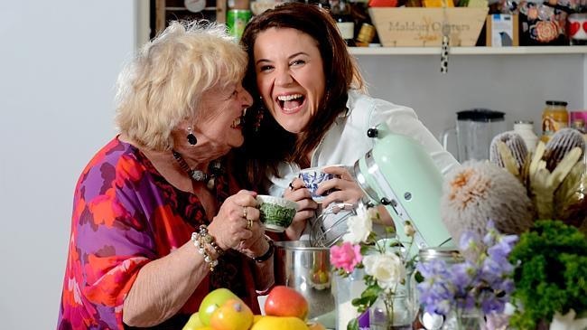 An old woman and a middle age woman holding tea cups and laughing.