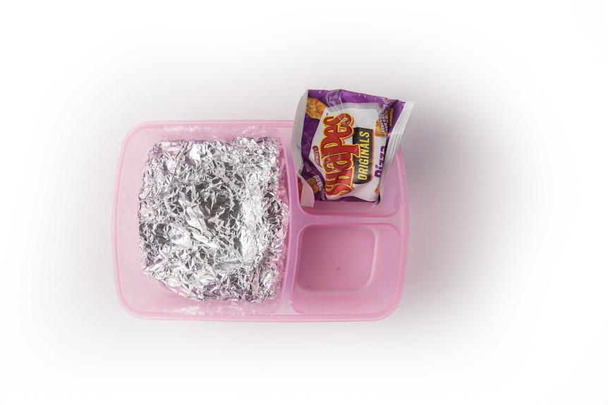 A jam and butter sandwich wrapped in foil and pizza-flavoured Shapes biscuits in a clear purple lunch box.