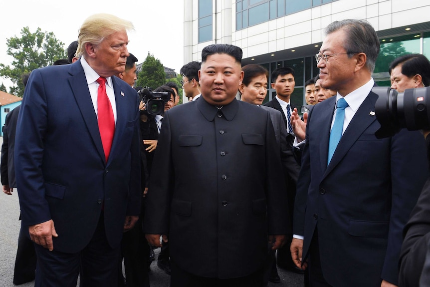 Three men stand side by side looking at each other.