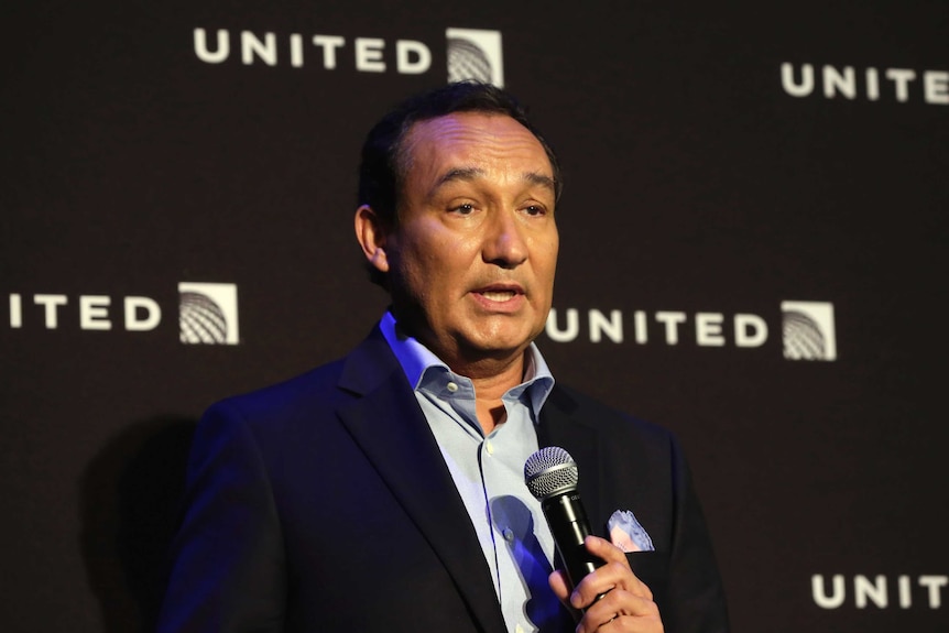 United Airlines CEO Oscar Munoz holds a microphone while delivering a speech in front of a United Airlines banner.