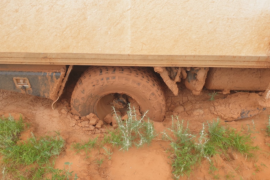 A campervan wheel is half-way in the dirt, covered in red mud.