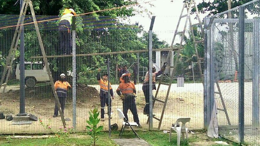 Workers in high-vis vests remove wires fences at Manus Island processing centre