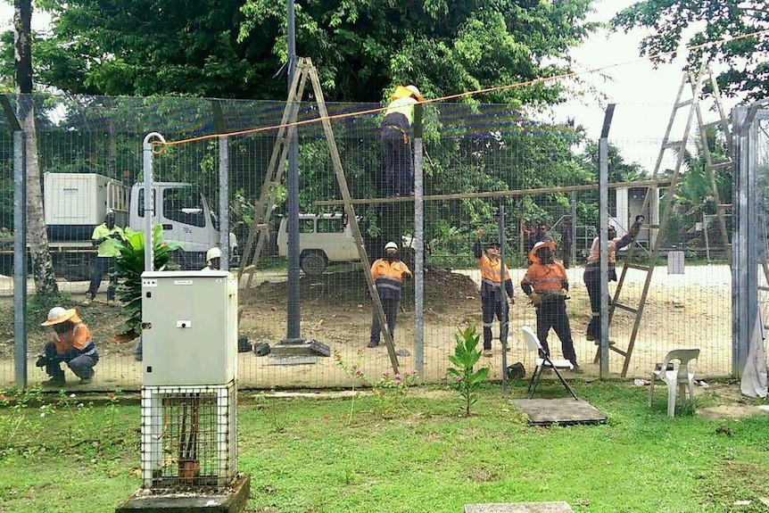 Workers in high-vis vests remove wires fences at Manus Island processing centre
